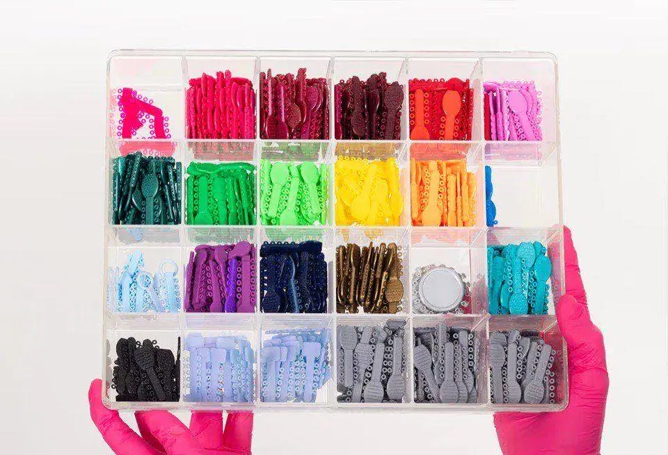 Gloved hands holding an open organiser tray filled with elastic ligature ties in more than twenty colours