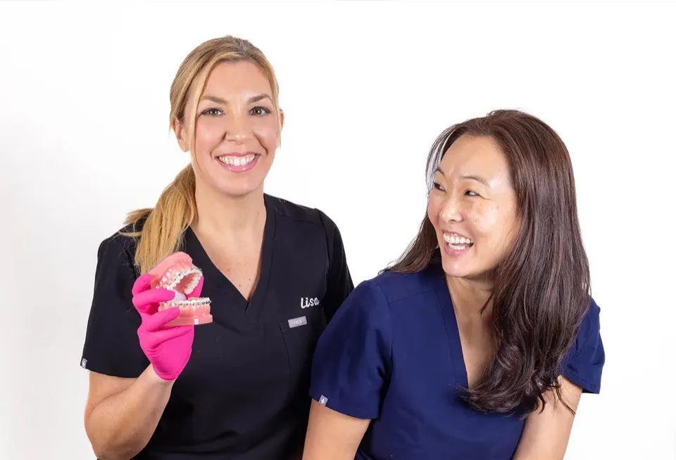 Two Wall Street Orthodontics team members smiling, one holding a dental model fitted with braces