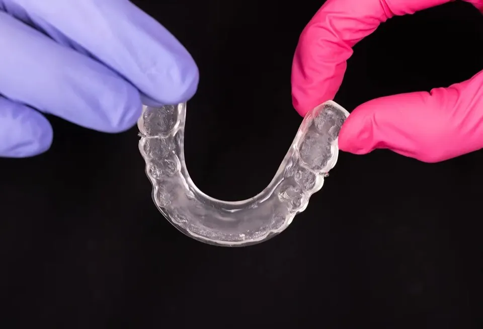 Two gloved hands holding a clear vacuum-formed retainer for the lower arch