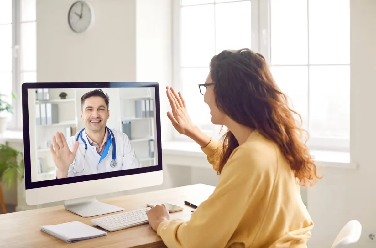 A patient at her desk waving to an orthodontist during a video consultation